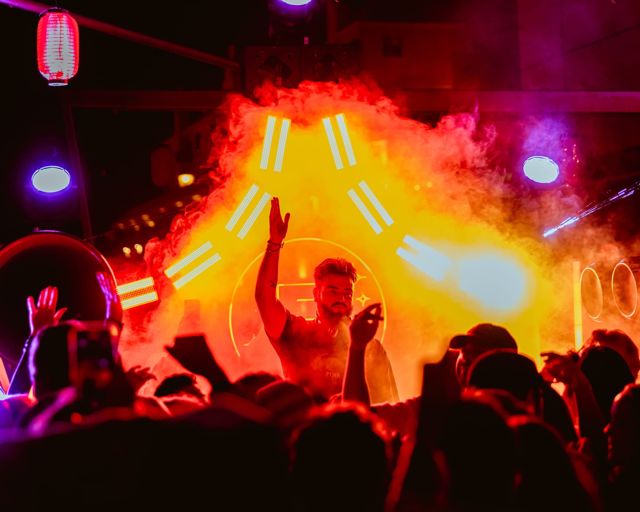 A DJ with one hand raised in orange smoke and stage light