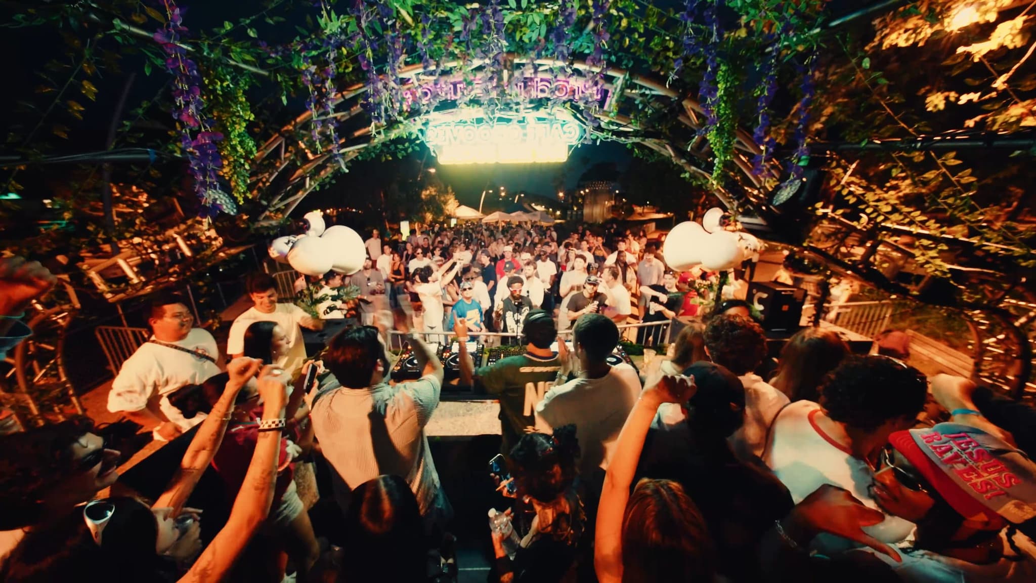View over the crowd toward the lit arch, inflatable swans floating above the dance floor