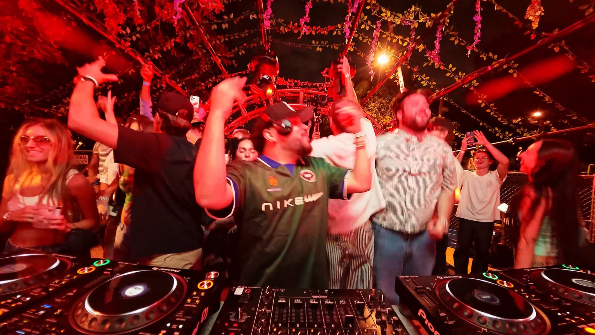 The DJ mid-set in a green jersey, the crowd behind him lit red