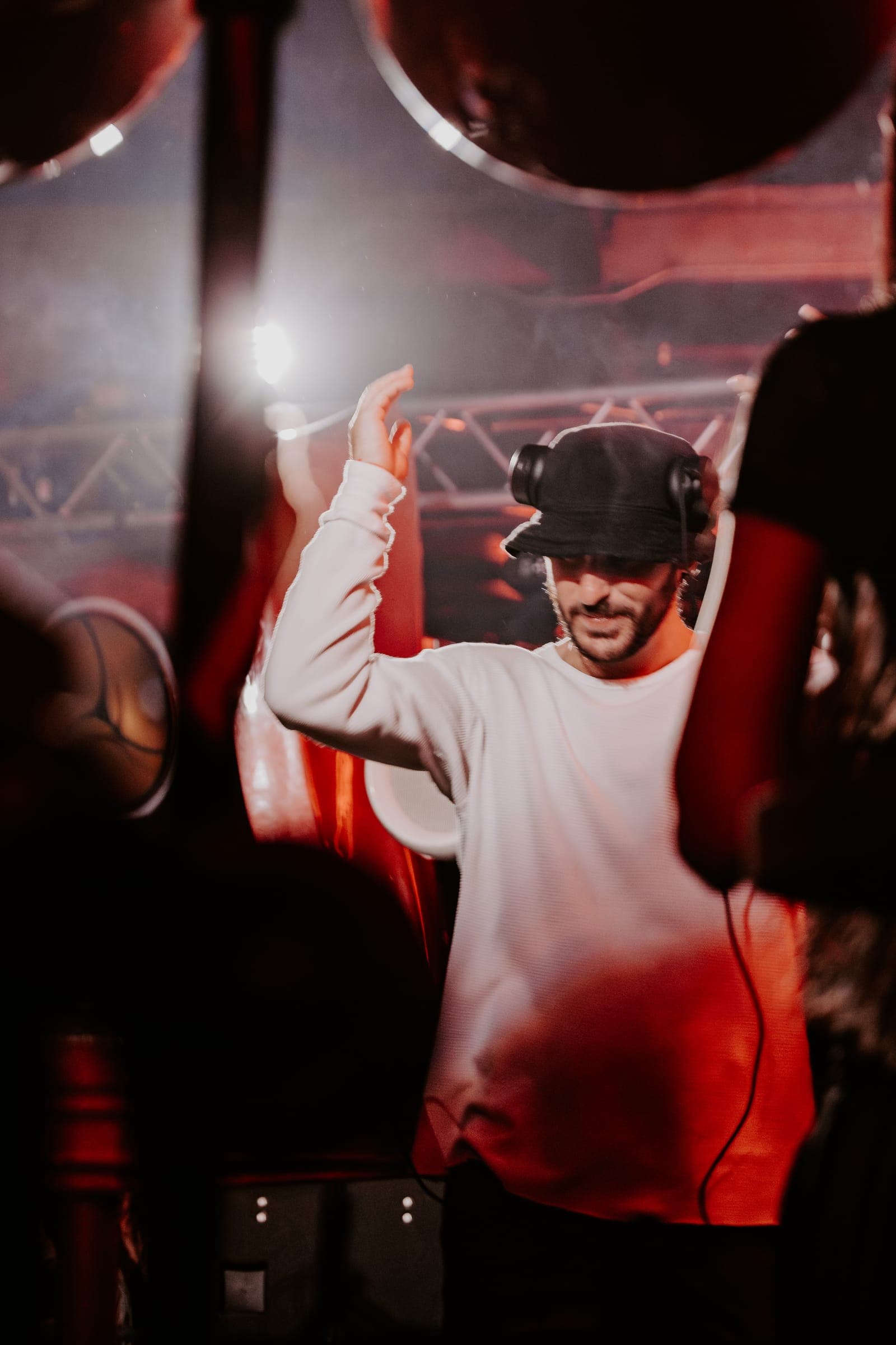 A DJ in a bucket hat and headphones raising one hand in red light