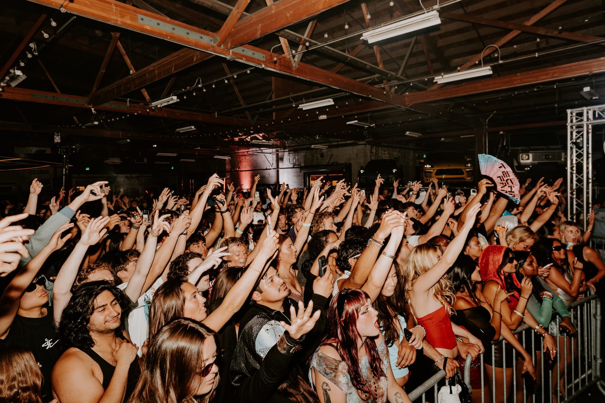 Front row at the barrier, dozens of hands reaching up under the warehouse rafters