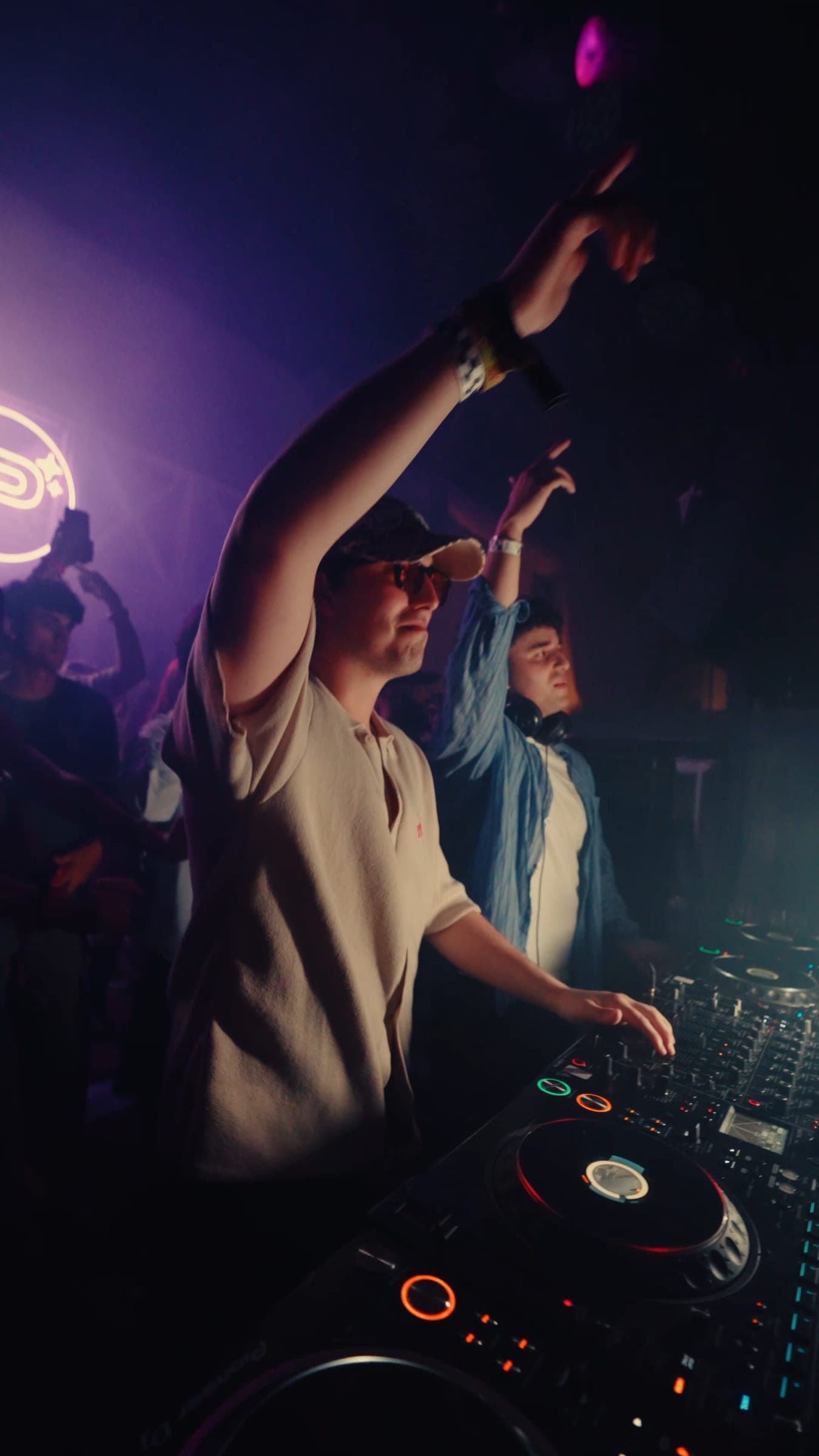 A DJ pointing at the ceiling mid-set, green light across the booth
