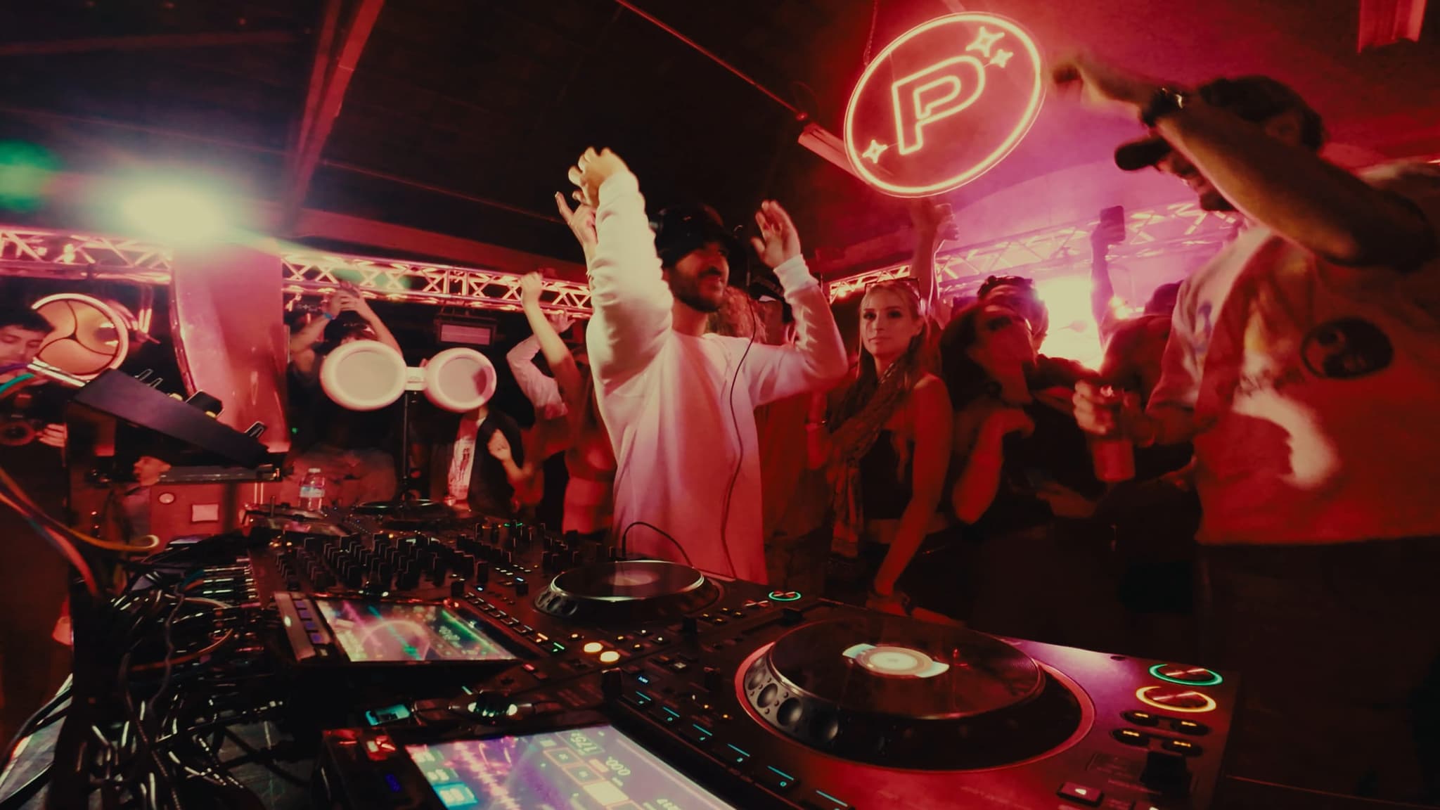 The DJ with both arms up beside the neon Product Pluto sign