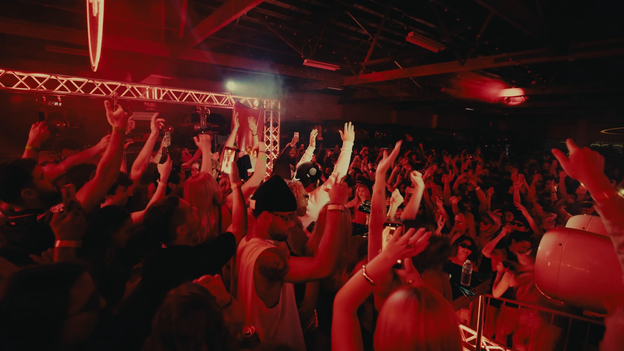 A red-lit crowd with hands in the air, seen from behind the booth