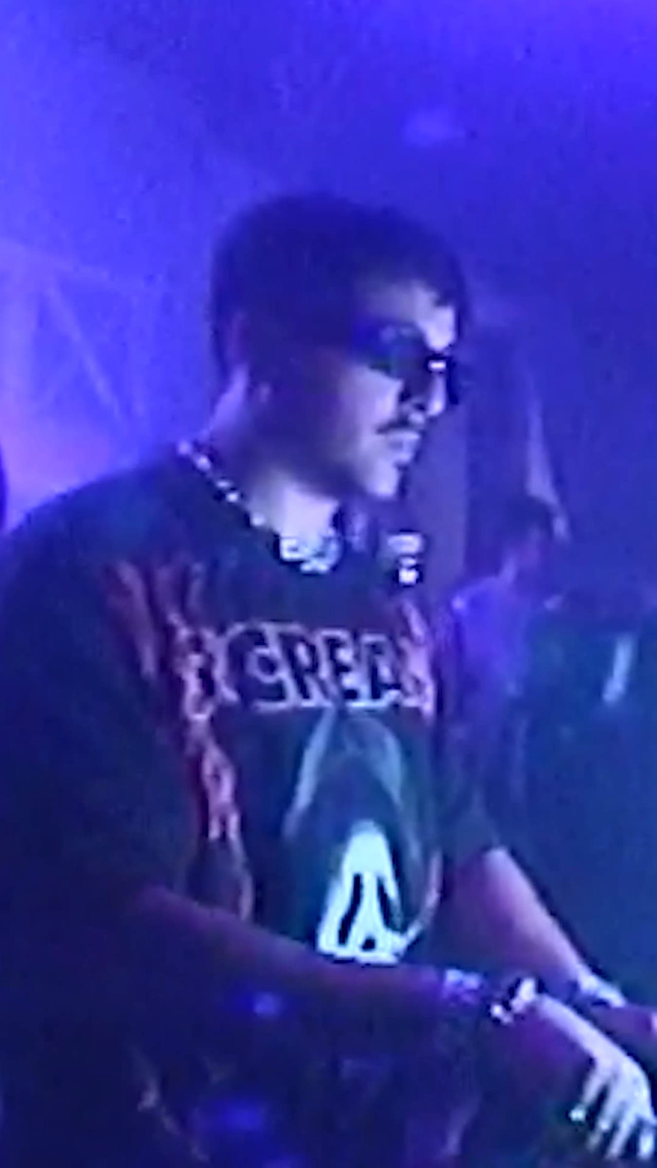 A DJ in sunglasses and a graphic tee at the decks under blue light